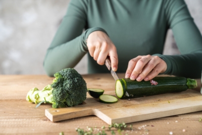 Jemand schneidet einen Bio-Zucchini neben Brokkoli.