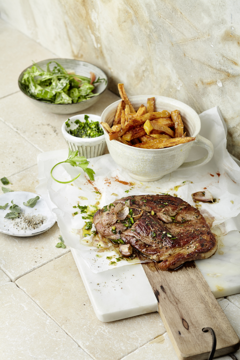 Lammsteak mit Bio-Süßkartoffelpommes & Kräutergremolata auf einem Tisch.