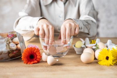 Jemand taucht Eierschalen in eine Schüssel Wasser, neben Ja! Natürlich Bio-Eiern.