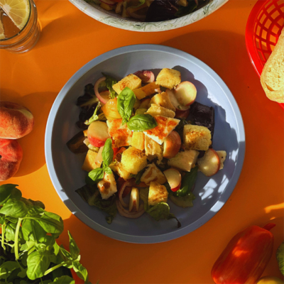 Hartweizen Panzanella mit Basilikum getoppt in einer Schale angerichtet. Drum herum firscher Basilikum, Tomaten und Pfirsiche