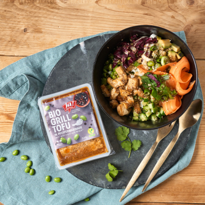 Bowl mit Tofu, Karotten, Edamame, Rotkraut und Reis. Daneben liegt der verpackte Tofu in Pfeffermarinade