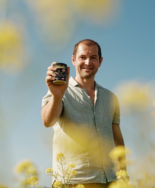 Landwirt mit Senf-Glas in der Hand und Blick in die Kamara