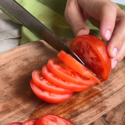 Bio-Tomate wird mit einem Messer in Scheiben geschnitte.