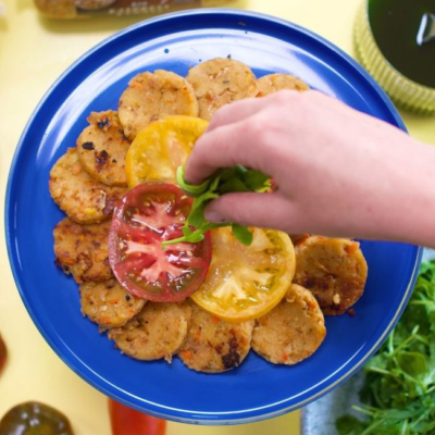 Gebratene Knödelscheiben auf einem Teller angerichtet und mit Rucola und Tomaten getoppt.