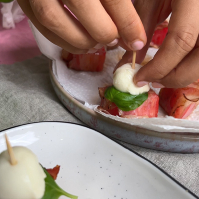 Melonen-Bacon-Stücke werden mit Mozzarella und Basilikum auf einen Spieß gespießt