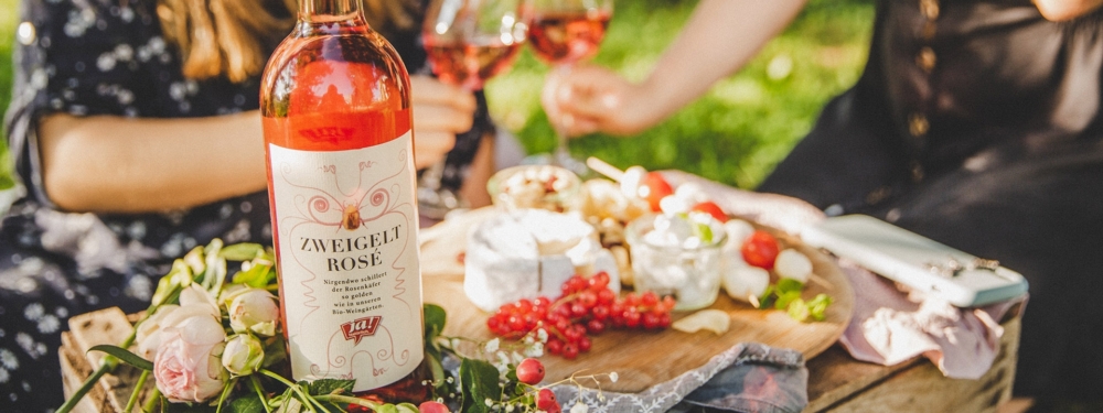 Eine Flasche Ja! Natürlich Bio-Zweigelt Rosé neben einer Jause auf einem Holzbrett.