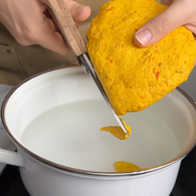 Teig mit einer Schere in kleine Nudeln direkt in das heiße Wasser schneiden