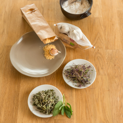 3 Teller stehen auf einem Tisch, auf einem ist getrockneter Knoblauch und auf den beiden anderen getrocknete Kräuter. Daneben eine Schüssel mit Speisestärke