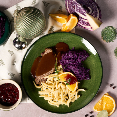 Braten auf einem Teller angerichtet mit Nockerl und Rotkraut