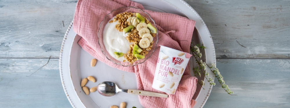Schüssel mit Ja! Natürlich Bio-Mandeljoghurt und einer Schüssel mit Joghurt, Granola und Früchten.