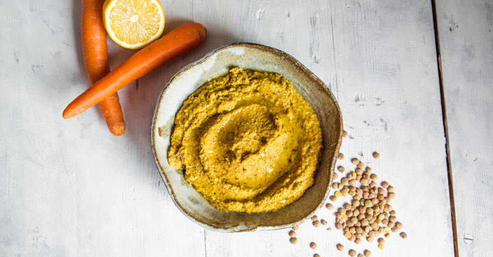 Linsenhummus in einer Schüssel mit Karotten und halber Zitrone auf hellem Hintergrund