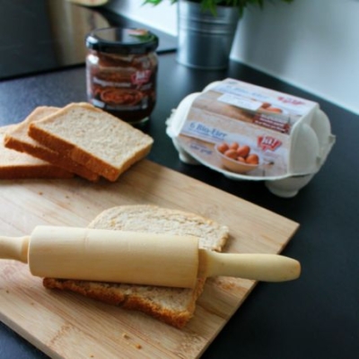 Jemand rollt eine Scheibe Toastbrot aus, dahinter Bio-Eier und Nougatcreme von Ja! Natürlich.