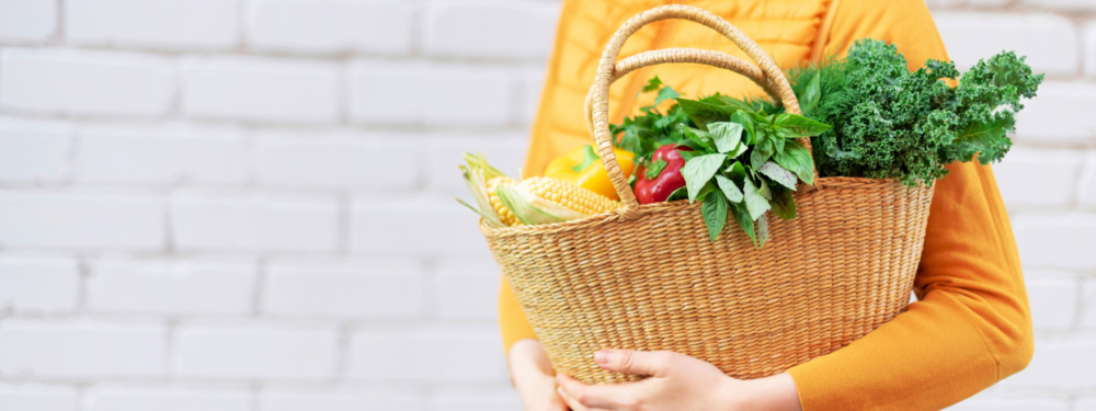 Jemand trägt Bio-Gemüse in einem Strohkorb.
