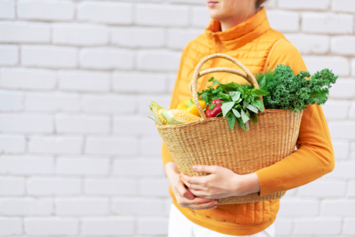 Jemand trägt Bio-Gemüse in einem Strohkorb.