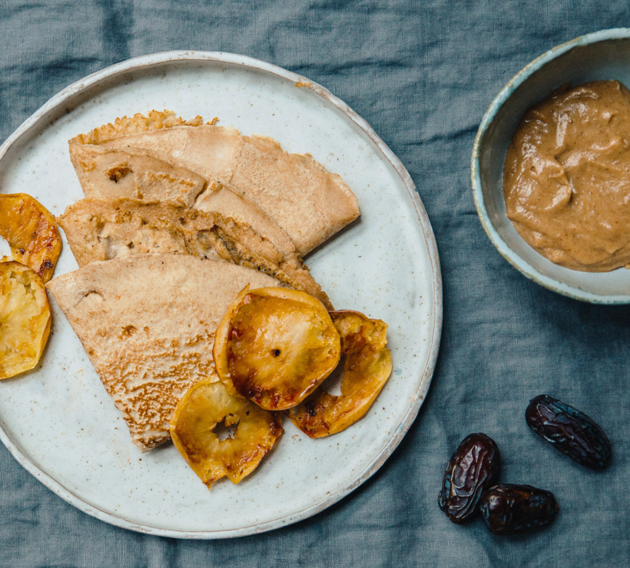 Bio-Dinkelvollkorn-Crêpes mit Mandelmus-Karamell und Bratäpfeln auf einem Teller.