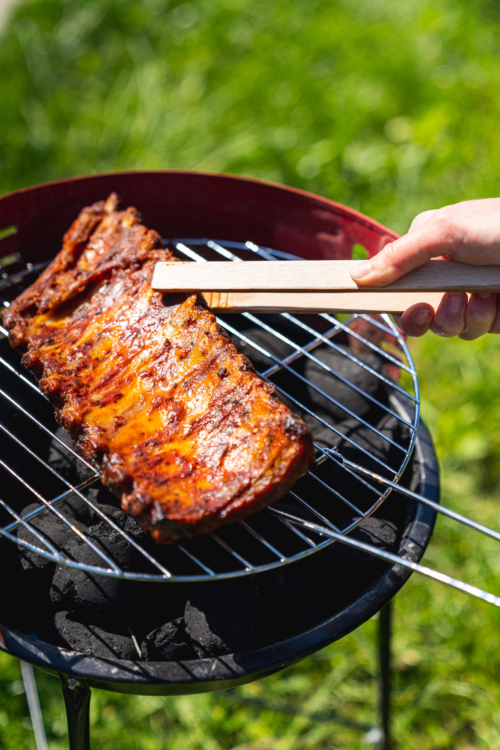 Eine Hand benutzt eine Zange, um Bio-Sparerips auf einem Grill im Freien zu grillen.