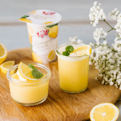 Ein Becher Ja! Natürlich Bio-Sommerfrisch Zitronen Joghurt mit Dessertschüsseln davor.