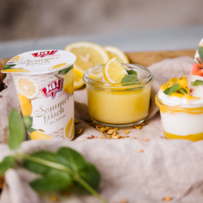 Ein Becher Ja! Natürlich Bio-Sommerfrisch Zitronen Joghurt mit Dessertschüsseln daneben.
