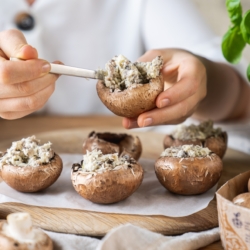 Jemand befüllt Bio-Champignons mit einer Frischkäsefüllung.