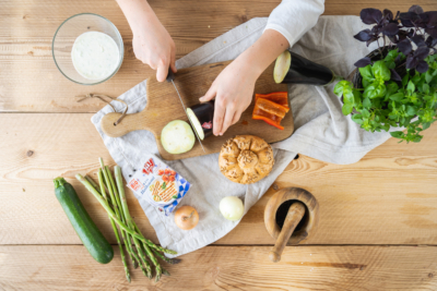 Jemand schneidet Zucchini, eine Packung Ja! Natürlich Bio-Halloumi und weiteres Gemüse liegt daneben.