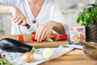 Jemand schneidet Bio-Gemüse, daneben eine Packung Ja! Natürlich Bio-Halloumi.