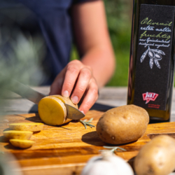 Jemand schneidet Bio-Erdäpfel. Im Hintergrund steht Ja! Natürlich Bio-Olivenöl.