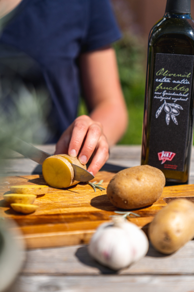 Jemand schneidet Bio-Erdäpfel. Im Hintergrund steht Ja! Natürlich Bio-Olivenöl.