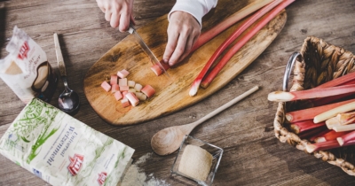 Jemand schneidet Bio-Rhabarber, drumherum Produkte von Ja! Natürlich.