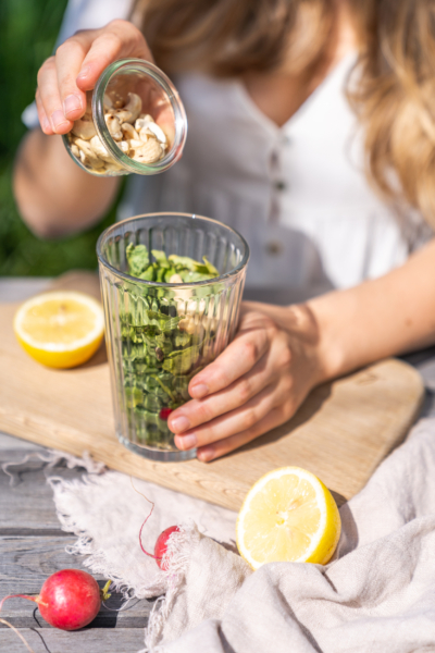 Jemand gibt Bio-Cashewkerne in ein Glas mit Radieschenblättern.