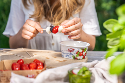 Jemand macht Spieße mit Ja! Natürlich Bio-Mozzarella, Paradeisern und Oliven.