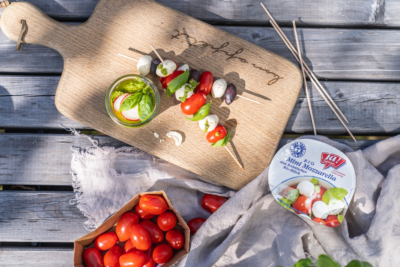 Spieße mit Ja! Natürlich Bio-Mozzarella, Paradeisern, Basilikum und Oliven auf einem Schneidebrett.