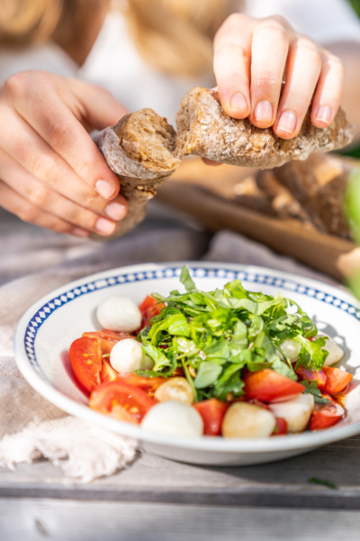 Jemand isst Bio-Brot mit einem Mozzarella-Tomaten-Salat.