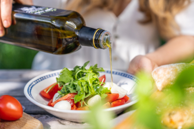 Jemand schüttet Olivenöl über einen Salat mit Mozzarella.