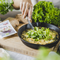 Jemand schneidet Frittata, daneben liegt Ja! Natürlich Bio-Feta.