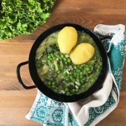 Ein Gusseisentopf mit eingebranntem Salat, zwei Bio-Erdäpfeln und Erbsen.
