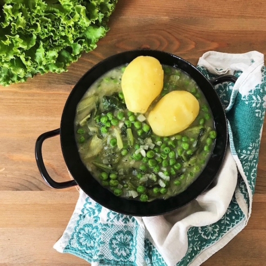 Ein Gusseisentopf mit eingebranntem Salat, zwei Bio-Erdäpfeln und Erbsen.