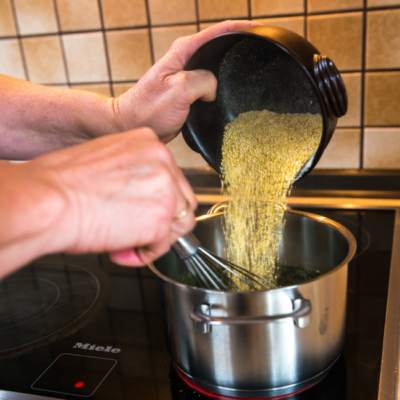 Jemand schüttet Bio-Hirse in einen Kochtopf.