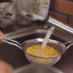 Jemand wäscht Bio-Hirse mit einem Sieb.