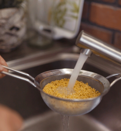 Jemand wäscht Bio-Hirse mit einem Sieb.