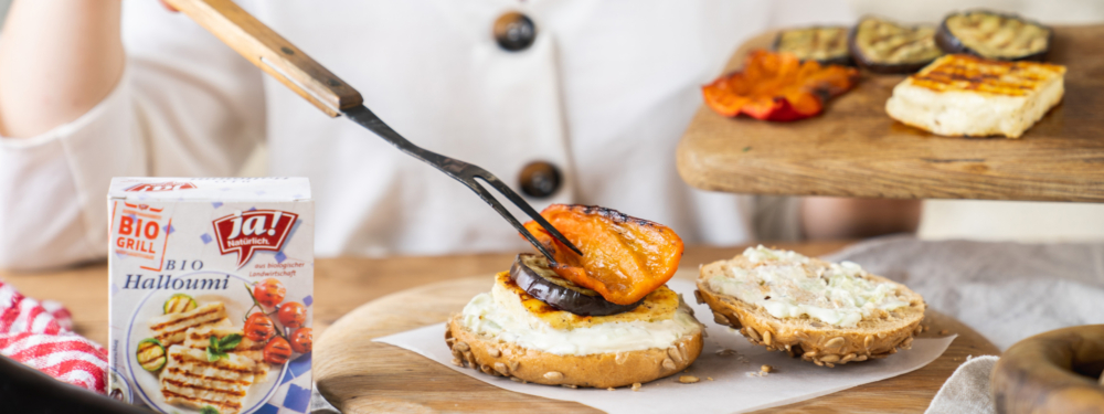 Ja! Natürlich Bio-Halloumi wird gemeinsam mit gegrilltem Gemüse auf einen Burger Bun gelegt.