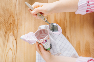 Jemand löffelt die Reste aus einem Ja! Natürlich Joghurtbecher.