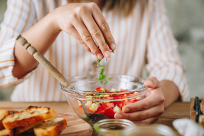 Jemand gibt Bio-Kräuter in eine Schüssel mit Gemüse.