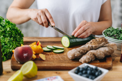 Jemand schneidet Bio-Zucchini auf einem Brett. Nebenbei ist weiteres Gemüse und Obst.