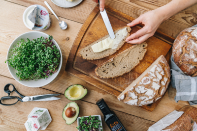 Jemand schmiert sich eine Scheibe Brot mit verschiedenen Bio-Produkten von Ja! Natürlich am Tisch.