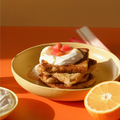 French Toast mit Rhabarberkompott auf einem Teller angerichtet mit frischen Orangen daneben