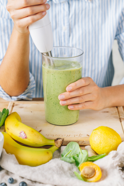 Jemand püriert einen grünen Smoothie, davor liegen Bio-Bananen und Zitronen von Ja! Natürlich.