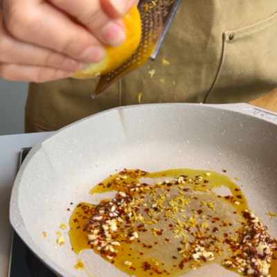 In einer Pfanne Bio-Olivenöl, Bio-Knoblauch, Bio-Chiliflocken und Bio-Zitronen-Abrieb anbraten.