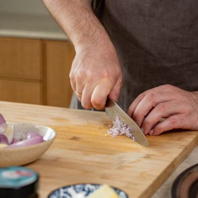 Bio-Schalotten werden fein auf einem Holzbrett geschnitten.