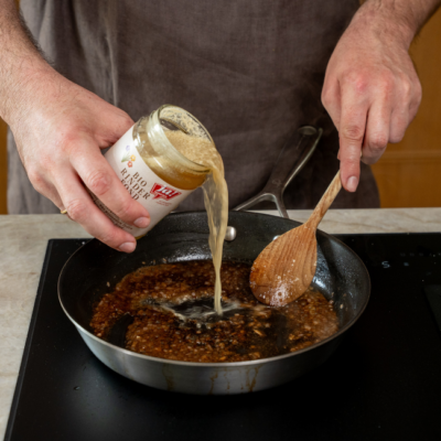 Bio-Rinderfond in eine Pfanne zu den Bio-Schalotten und dem Bio-Knoblauch gießen.