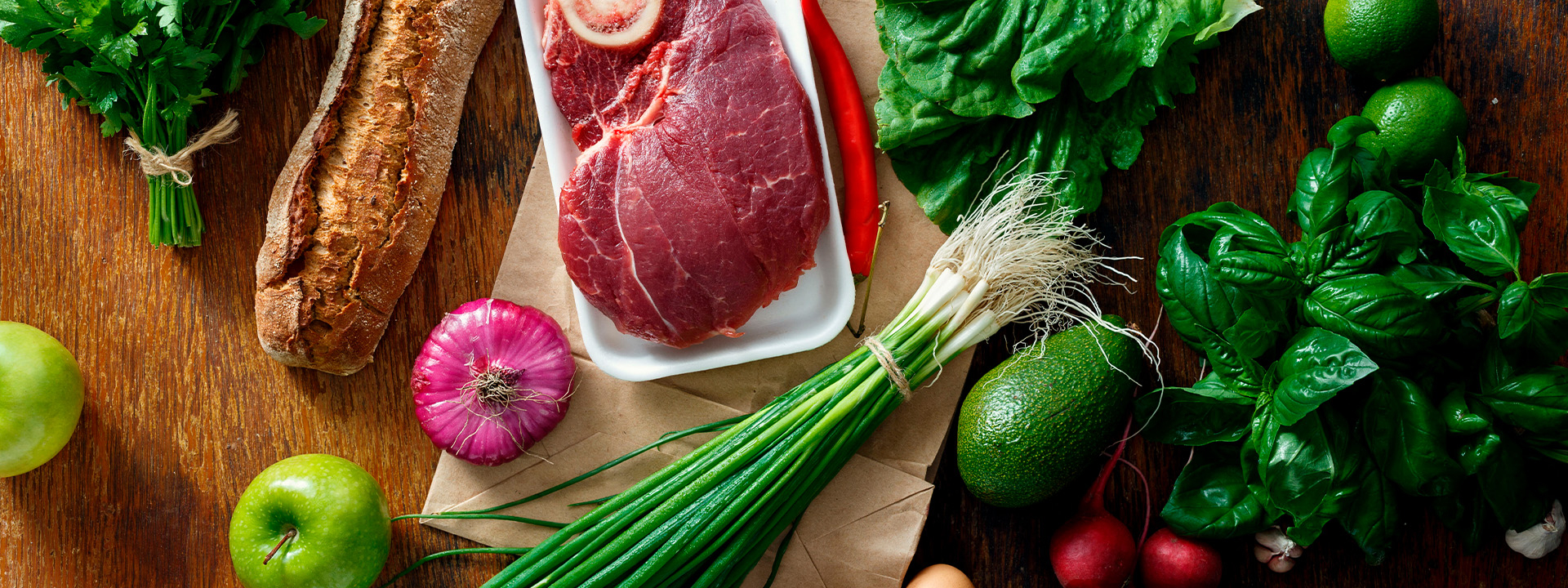 Bio-Gemüse, Bio-Fleisch, Bio-Kräuter und Bio-Brot nebeneinander auf einem Tisch.